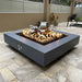 A gray outdoor square concrete fire pit with a vibrant flame placed on a tiled surface modern outdoor patio