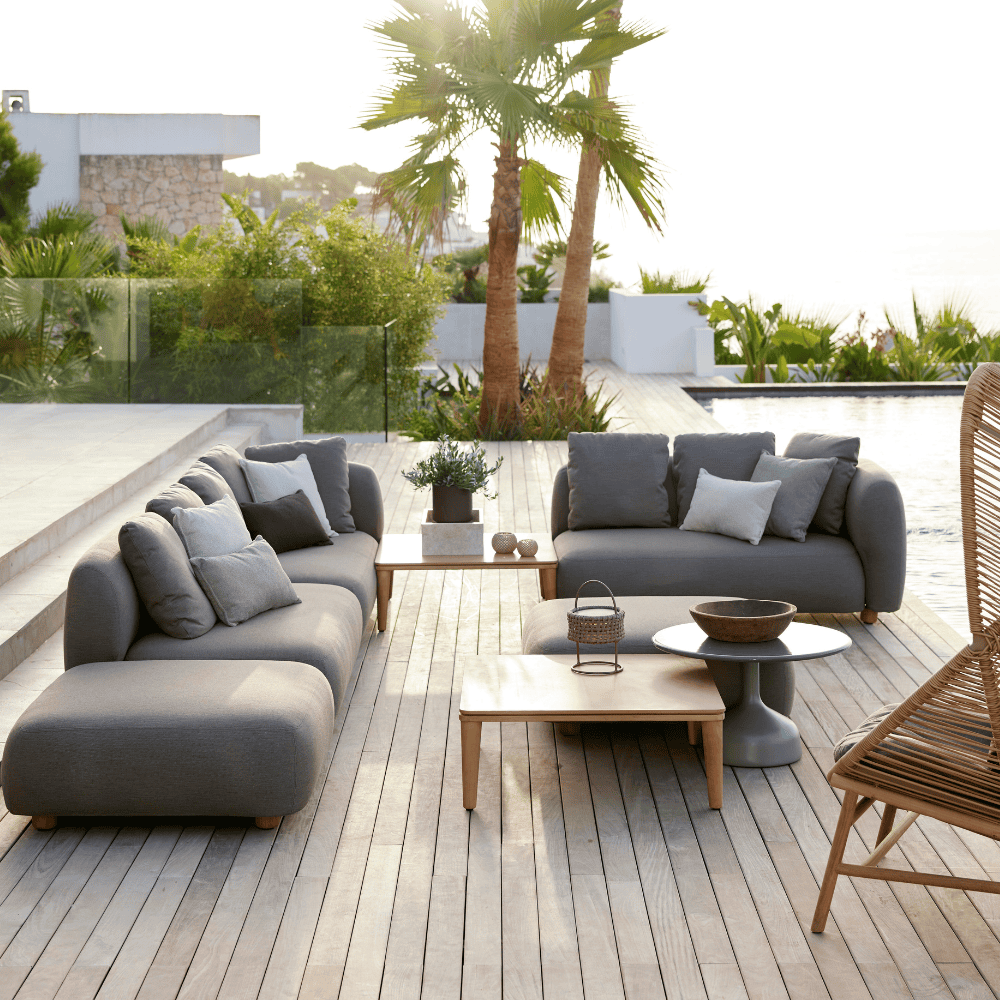 Boxhill's Capture Outdoor Pouf lifestyle image with Capture Module Sofa and Capture Coffee Table on wooden platform beside the pool