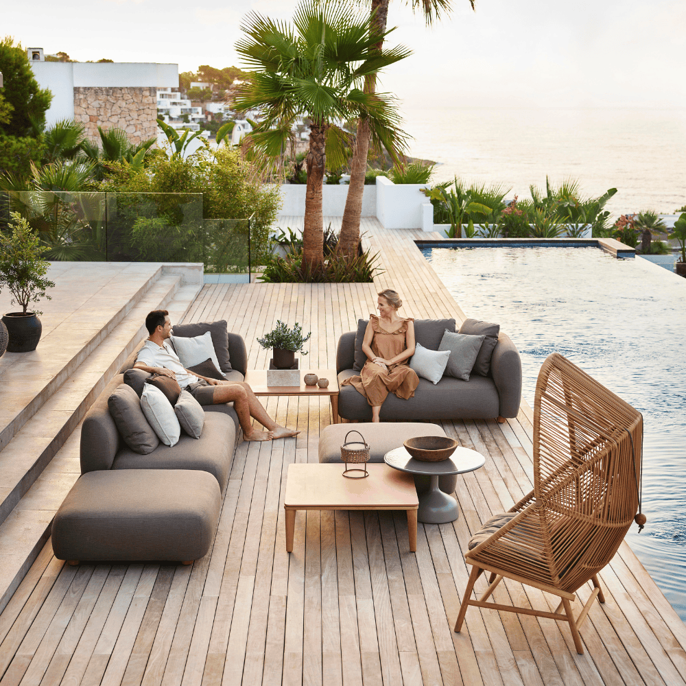 Boxhill's Capture Outdoor Pouf lifestyle image with Capture Module Sofa and Capture Coffee Table beside the pool with 2 people sitting down