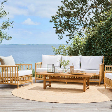 A coastal outdoor seating area features a rectangular teak coffee table with a slatted top and surrounding sofas.