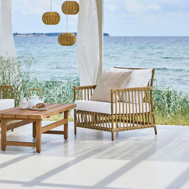 Natural woven rattan outdoor lounge chair with white cushions in a covered waterfront patio setting.