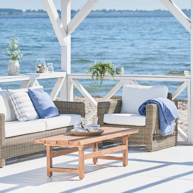 Gray woven rattan outdoor lounge chair with white cushions in a covered waterfront patio setting.