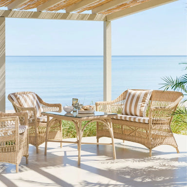 Rectangular natural woven rattan outdoor lounge sofa with striped cushions in a covered waterfront patio setting.