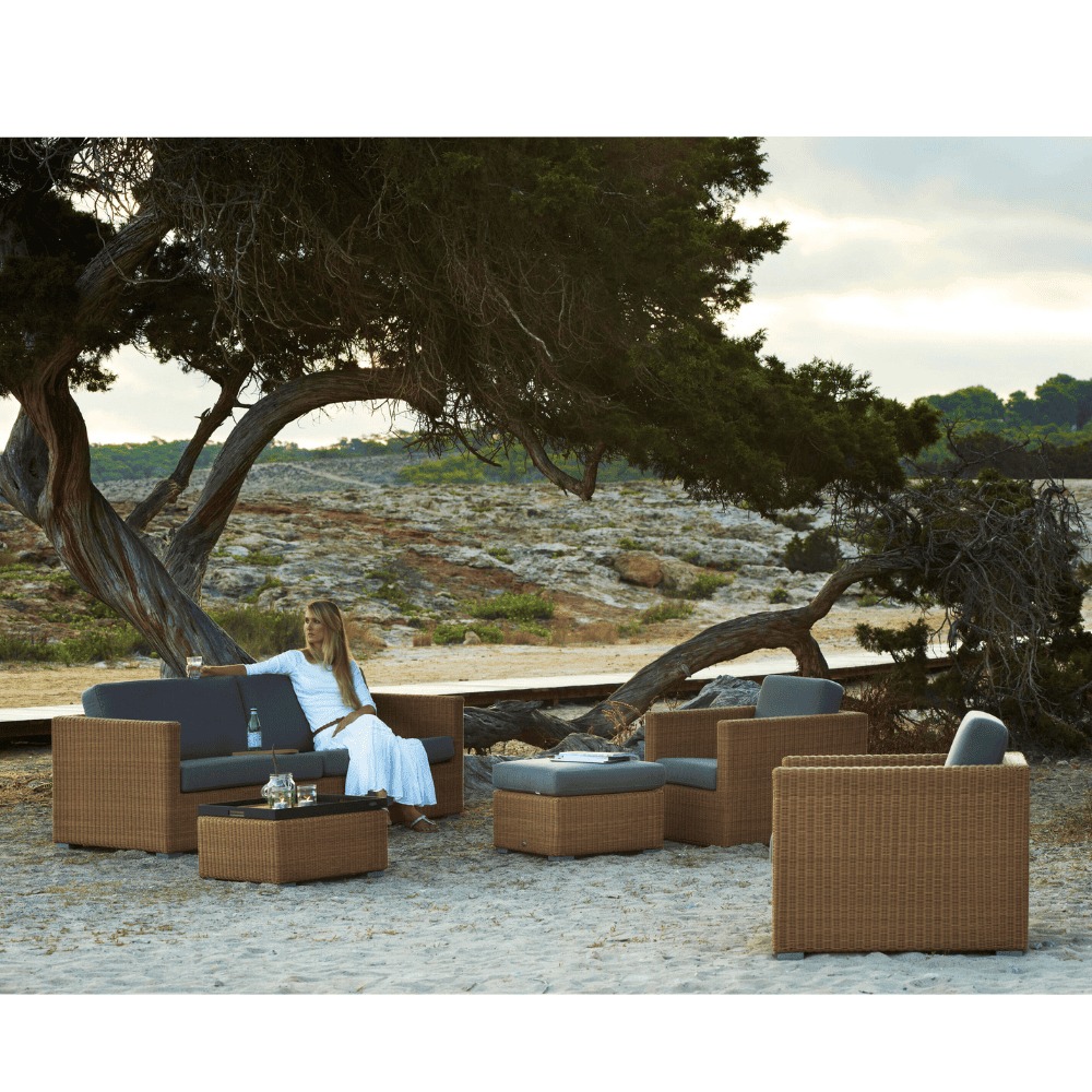 Boxhill's Chester 3-Seater Coastal Sofa Natural with Chester Footstool Weave Coffee Table and Chester Lounge Weave Coastal Chair lifestyle image beside the tree with a woman sitting down