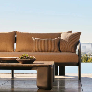 Brown outdoor 3 seater sofa with pillows and a coffee table set on a tiled patio