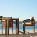 Two brown modern dining armchairs and a rectangular outdoor dining table are placed on a tiled surface beside the pool