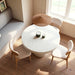 Top view of interior dining area with round white concrete outdoor dining table, three wooden chairs with white cushions, gray bench and woven pendant light