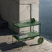 Green metal patio serving cart placed against glass railing on a wooden deck balcony beside glass railings