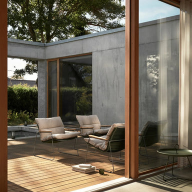 Four modern outdoor lounge chairs with wooden armrests and beige cushions on a wooden deck patio