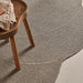 Outdoor rug in brown woven material with textured pattern, styled with wooden stool