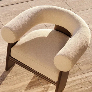 Modern light beige outdoor lounge chair with curved barrel-back bolster and dark brown  aluminum frame on a tiled floor.