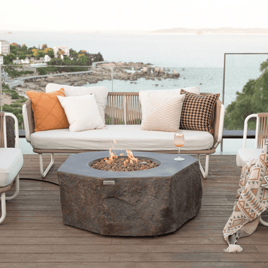 Brown hexagonal shaped outdoor concrete fire pit table surrounded by white sofa and chairs on a wooden deck outdoor patio