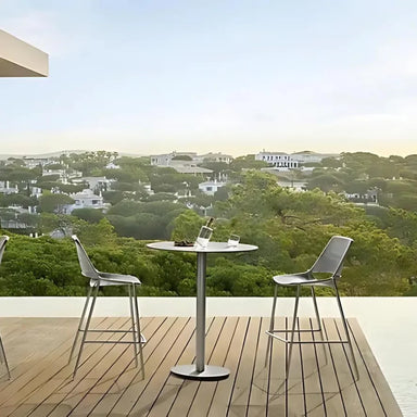 Two silver gray steel mesh armless stackable bar stools and a round bar table set on a wooden deck patio with a scenic view of a residential area