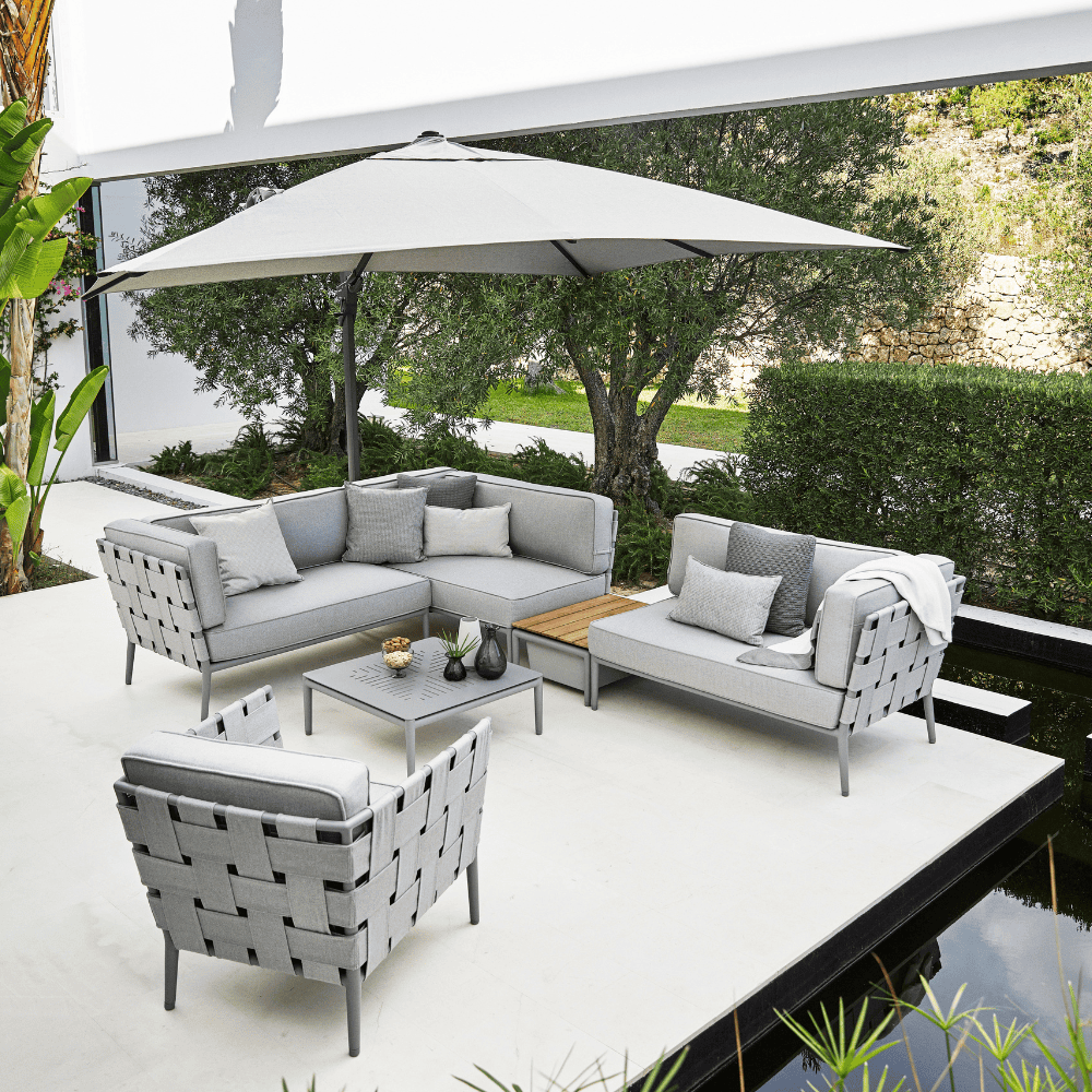 Boxhill's Conic Outdoor Coffee Table Light Grey lifestyle image with Conic Sectional Sofa, Conic Lounge Chair, Conic Box Outdoor Storage Table, and big umbrella sunshade at patio