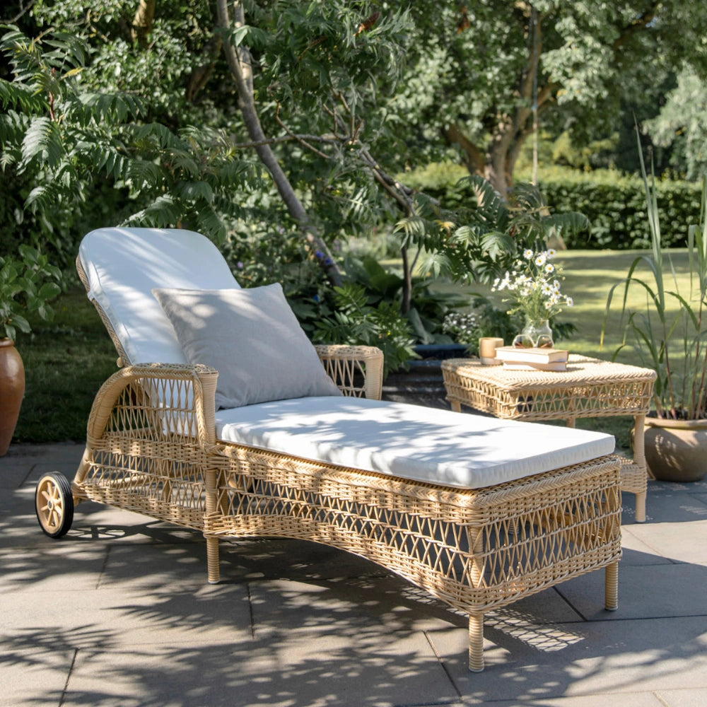 Natural wicker outdoor sunbed with adjustable backrest, rear wheels and white cushions beside a matching side table.