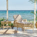 Natural wicker outdoor sunbed with striped beige and white cushions beside a matching wicker side table.