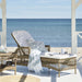 Natural wicker outdoor sunbed with white cushions, rear wheels and matching side table overlooking the ocean.