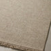 Close-up of a woven outdoor rug or textile in a warm beige/tan color with a short fringe along one edge, shown against a light neutral background.