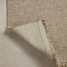 Close-up of a woven natural-fiber outdoor rug in a warm beige tone, with one corner folded over to show the underside and fringed edge.