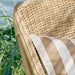Close-up of a natural wicker outdoor 3-seater sofa with a striped beige and white cushion.