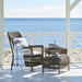 Grey wicker outdoor armchair with white and blue striped cushions beside a matching woven stool and side table.