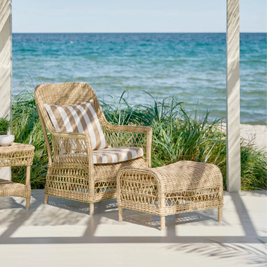 Natural wicker outdoor armchair with striped beige and white cushions and matching woven stool.