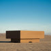 A brown outdoor square concrete fire pit table placed on a cracked dry desert ground