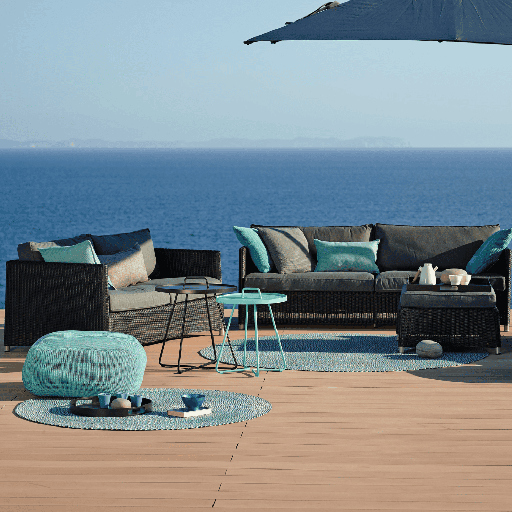 Boxhill's Diamond 2-Seater Weave Sofa lifestyle image with Diamond 3-Seater Weave Sofa and Diamond Weave Footstool on wooden platform at seafront