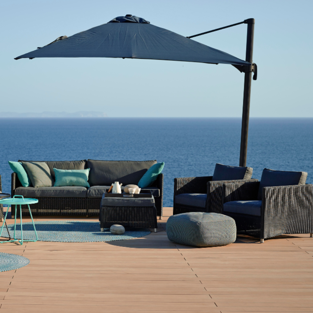 Boxhill's Diamond Weave Lounge Chair lifestyle image with Diamond 3-Seater Weave Sofa, Diamond Weave Footstool and parasol on wooden platform at seafront