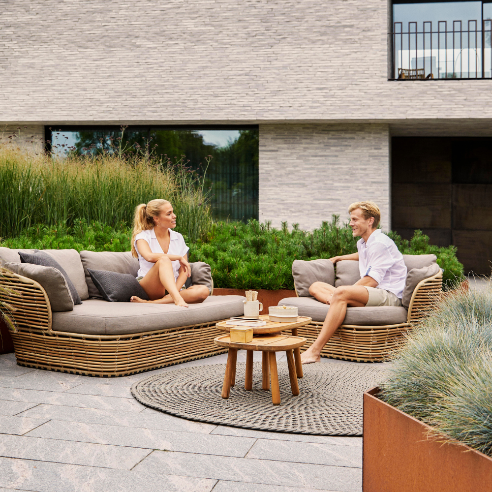 Boxhiil's Discover Round Outdoor Rug Taupe lifestyle image with a woman sitting on a sofa and man sitting on lounge chair