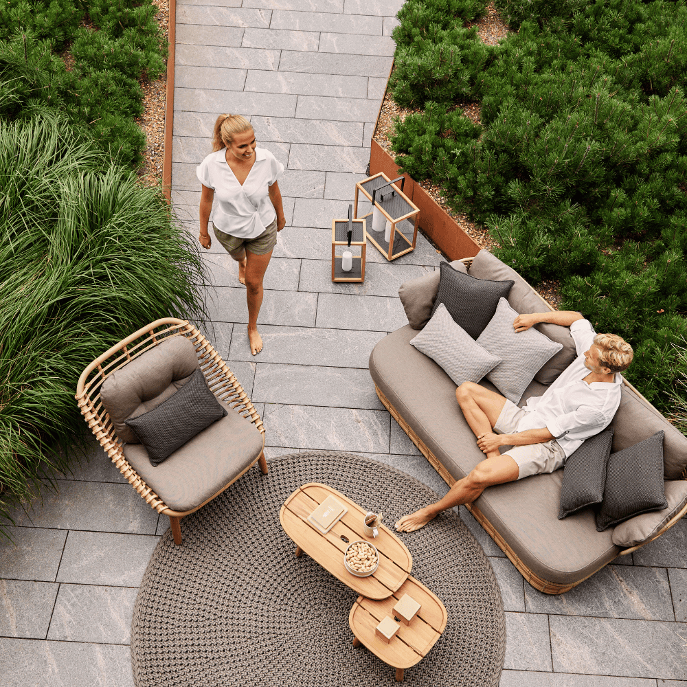 Boxhiil's Discover Round Outdoor Rug Taupe lifestyle image with a man sitting on a sofa and woman standing beside lounge chair