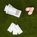 A set of white dominoes with pale blue-gray pips and a small pile of pink-and-white striped dominoes, arranged on green artificial grass.