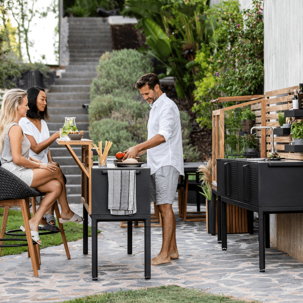Boxhill's Drop Outdoor Kitchen Module with 3 Shelves lifestyle-image at patio with 2 women sitting down and man standing beside preparing some food