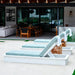 Three modern outdoor lounge chairs with white frames and light blue cushions arranged on a patio in front of a contemporary house.