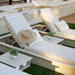 Outdoor chaise lounge chairs with light beige and white geometric patterned cushions, set on a patio with small side tables, potted plants, and a straw hat resting on one chair.