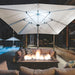 A large cream patio umbrella with a central integrated LED light casting a warm glow over an outdoor fire pit table on a modern patio at night.