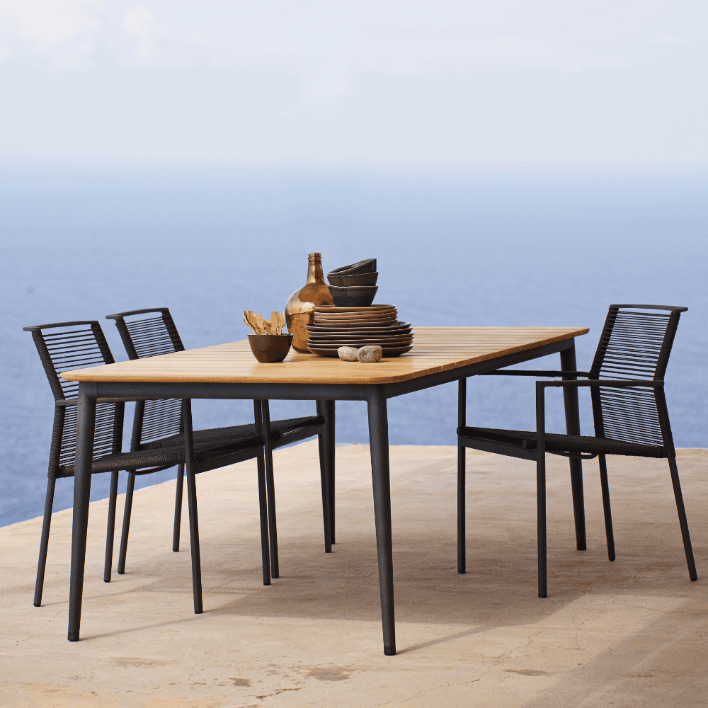 Boxhill's Edge Stackable Outdoor Armchair lifestyle image with teak top dining table at seafront