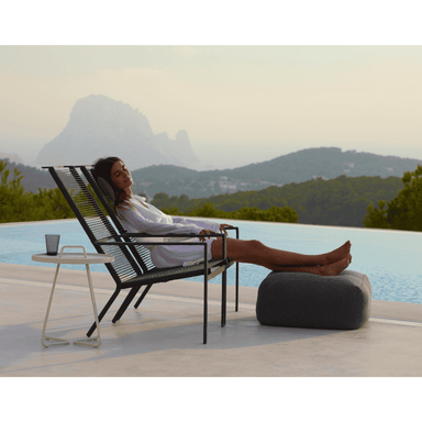 Boxhill's Edge Stackable Pool Side Highback Chair lifestyle image beside the pool with round side table, Divine Fabric Footstool and a woman sitting down