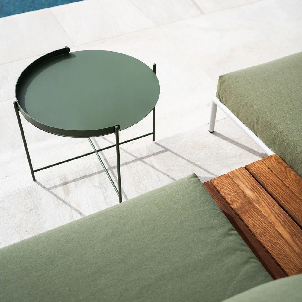 Green round patio tray table placed in front of a green sofa with a wooden side table, on a tiled floor beside the pool