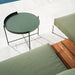 Green round patio tray table placed in front of a green sofa with a wooden side table, on a tiled floor beside the pool