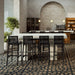 Two white rectangular concrete outdoor bar tables with black high chairs, patterned tile floor and pendant lights in modern interior setting