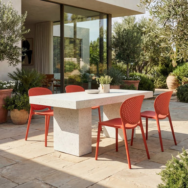 Patio dining with white rectangular concrete outdoor dining table and four orange side chairs, surrounded by greenery