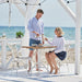 Two people enjoying a meal at a natural rattan outdoor dining table with matching white side chairs by the beach.