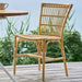 Natural rattan outdoor dining side chair beside a wooden dining table on a seaside deck.
