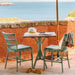 Green rattan outdoor dining side chairs with a wooden pedestal table on a seaside terrace.