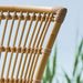 Close-up of a natural rattan outdoor dining side chair featuring an open slatted backrest.