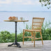 Natural rattan outdoor dining side chair beside a matching pedestal table on a wooden deck overlooking the ocean.