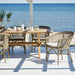 Grey rattan outdoor dining side chairs with a matching wooden dining table overlooking the ocean.
