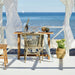 Grey rattan outdoor dining side chair with a matching wooden table overlooking the ocean.