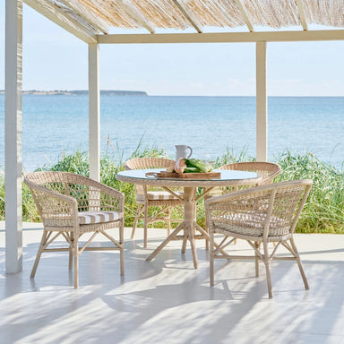 Natural rattan outdoor dining side chairs with a matching round dining table overlooking the ocean.